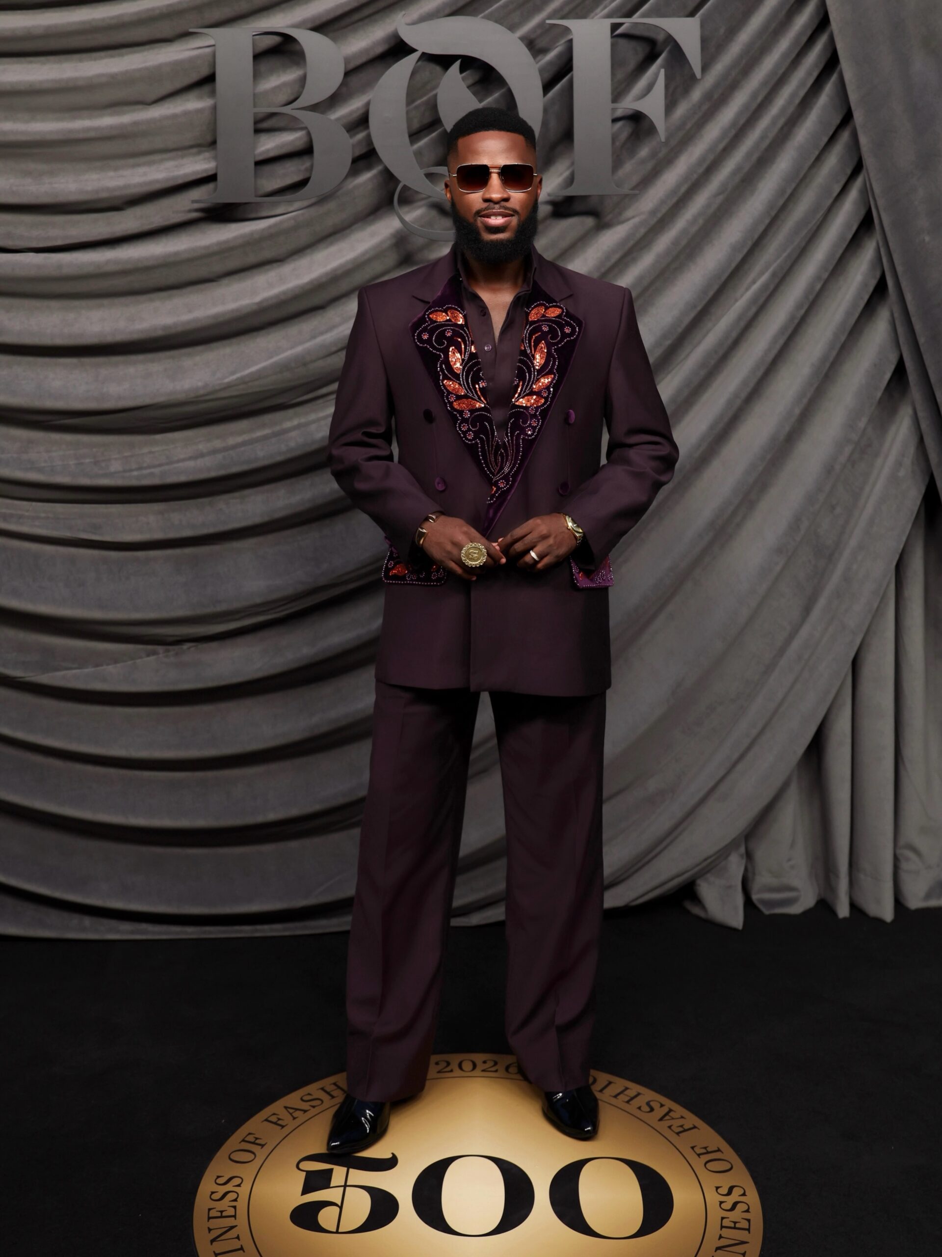 Dr Akin Faminu wearing custom Deji and Kola deep plum double-breasted suit with copper leaf embroidery at the Business of Fashion BoF 500 Gala in Paris.