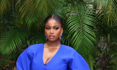 Temi Nkem wearing blue statement drop earrings, a wide gold cuff bracelet, glossy nude lip makeup, and holding a royal blue fringe clutch purse.