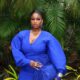 Temi Nkem wearing blue statement drop earrings, a wide gold cuff bracelet, glossy nude lip makeup, and holding a royal blue fringe clutch purse.