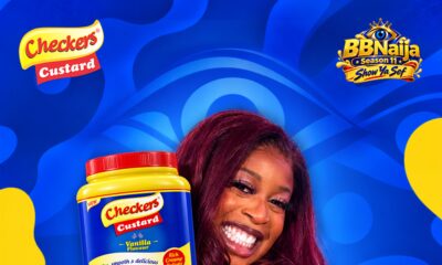 BBNaija Season 11 winner Temi Nkem holding a 2kg jar of Checkers Custard Vanilla Flavour against a blue background.