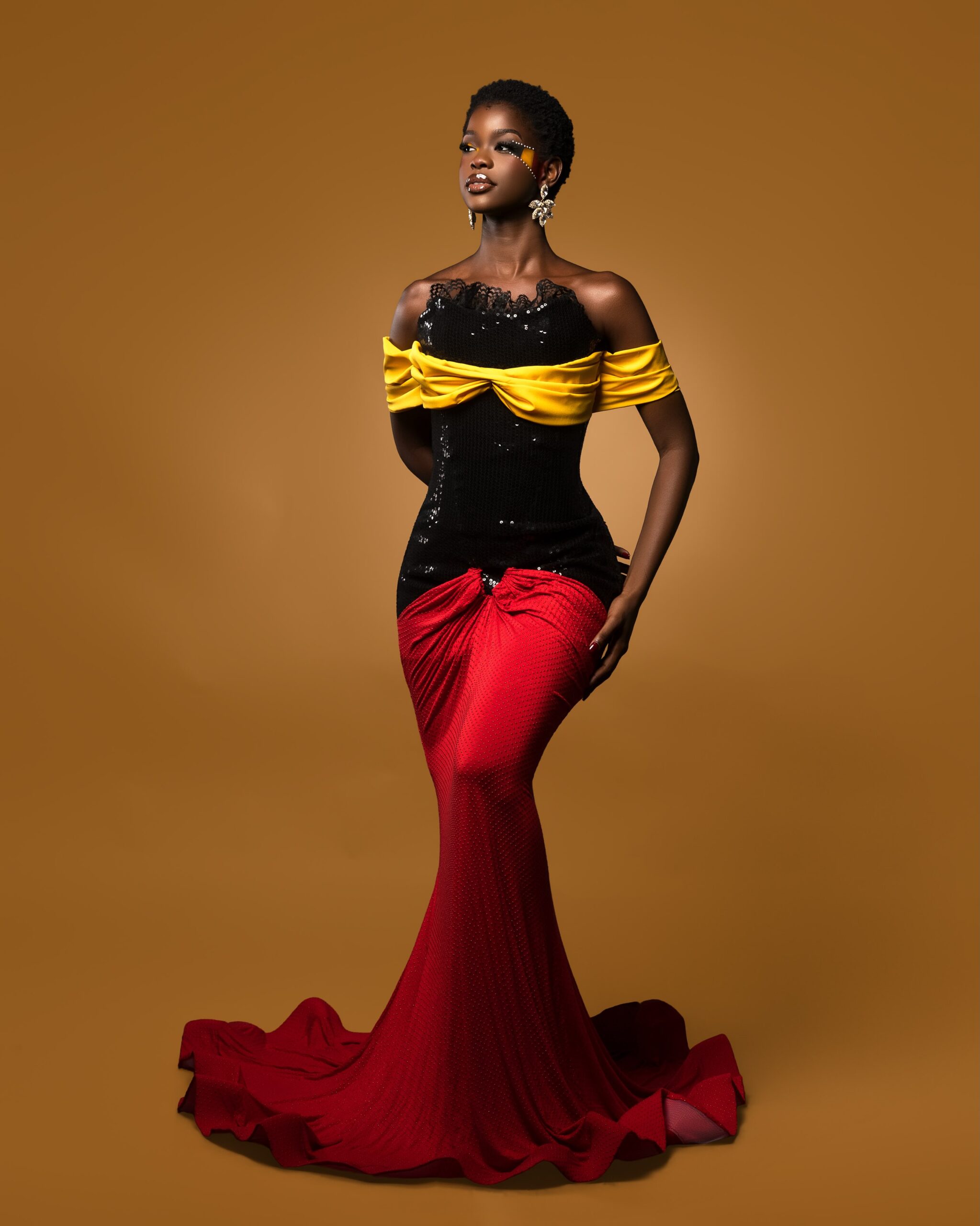 Kimberly Jael wearing a black sequined corset gown with yellow draping and a long red train celebrating Uganda Independence Day.