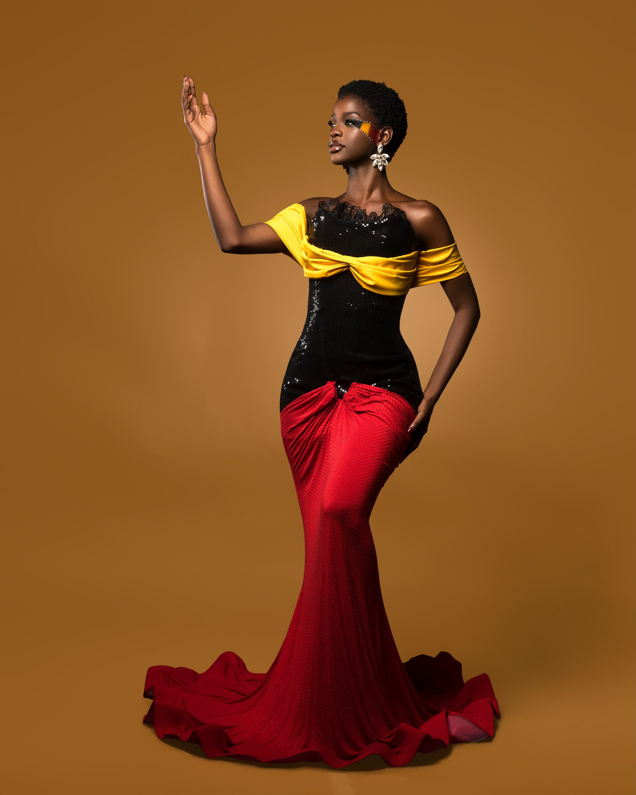 Kimberly Jael posing in a black, yellow, and red evening gown for Uganda Independence Day.