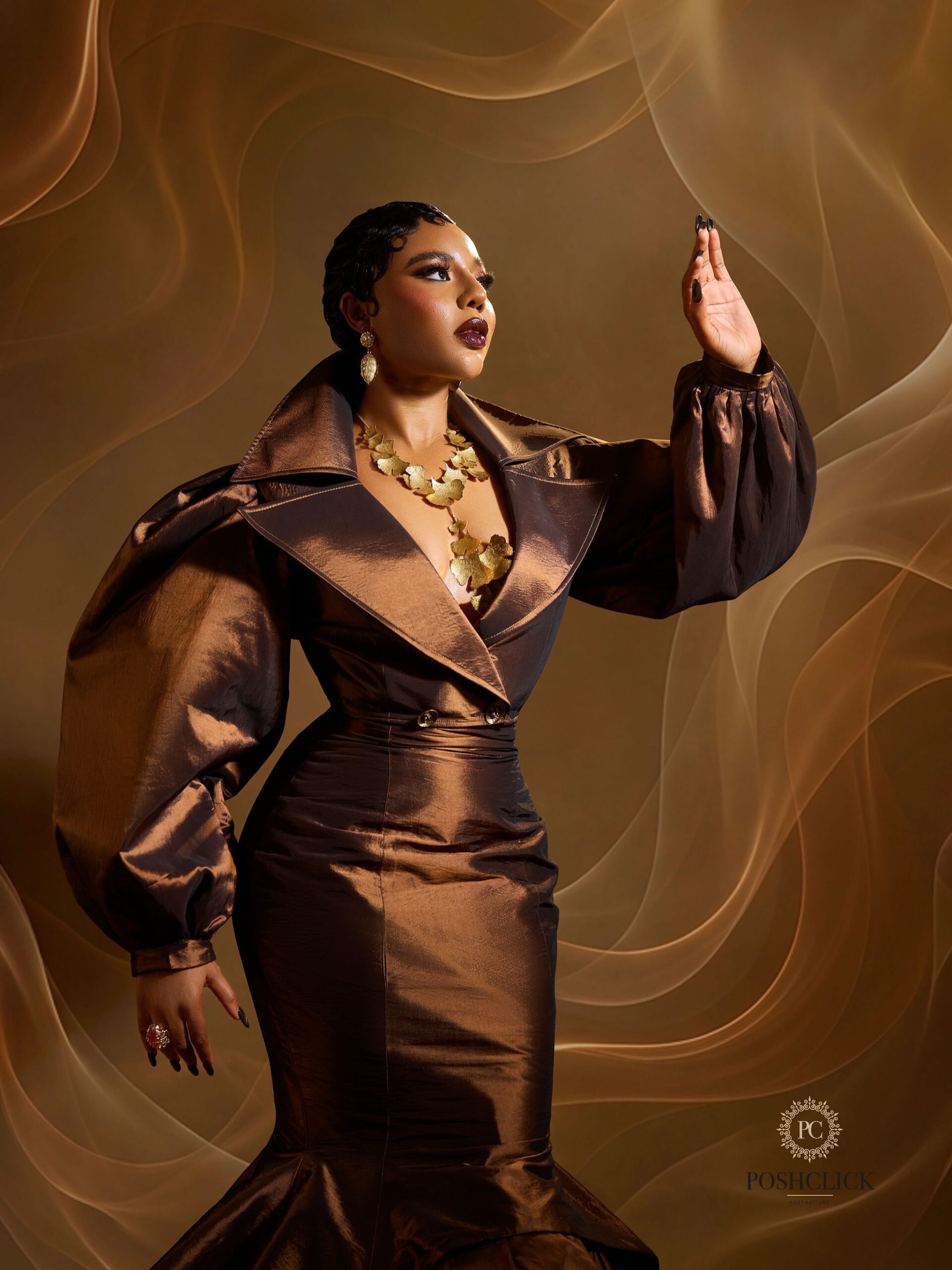 Nancy Isime posing in a metallic brown dress with an oversized collar, balloon sleeves, and a gold leaf necklace.