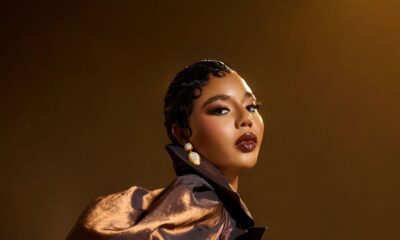 Nancy Isime featuring finger-wave hair, glossy dark lip liner, and pearl gold earrings in a metallic brown outfit.
