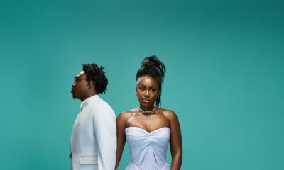 Zlatan Ibile holding hands with Davita Omoniyi against a teal backdrop in pastel ice blue and blush pink outfits.