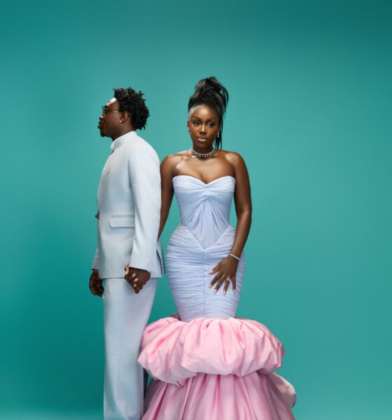 Zlatan Ibile holding hands with Davita Omoniyi against a teal backdrop in pastel ice blue and blush pink outfits.