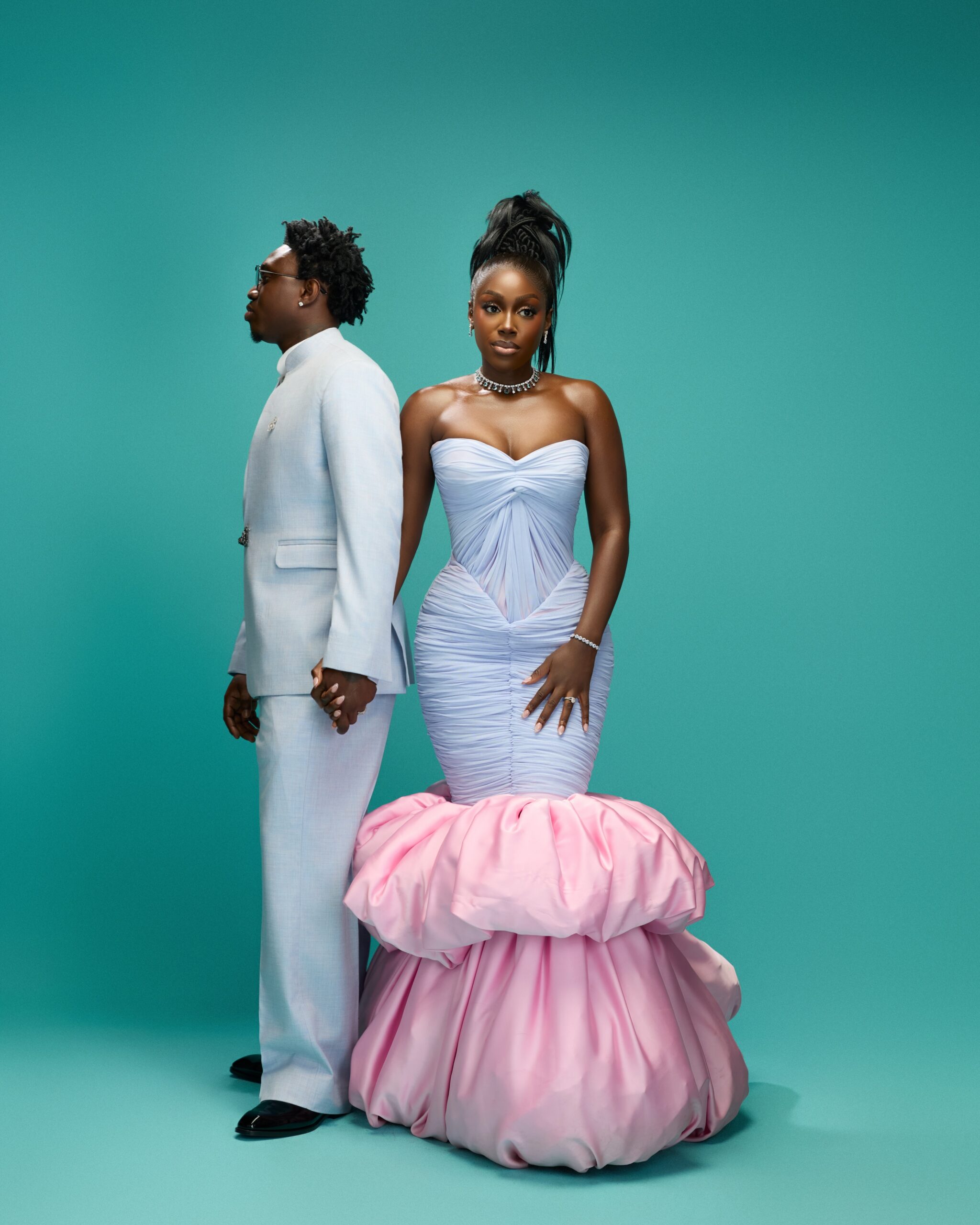 Zlatan Ibile holding hands with Davita Omoniyi against a teal backdrop in pastel ice blue and blush pink outfits.