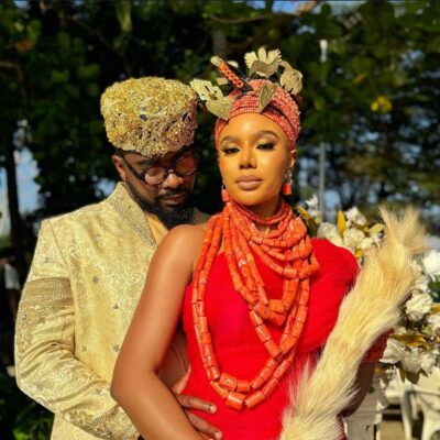 Uzor Arukwe in a gold brocade outfit standing behind Nancy Isime in red traditional Edo attire and coral beads for Loving Itohan.