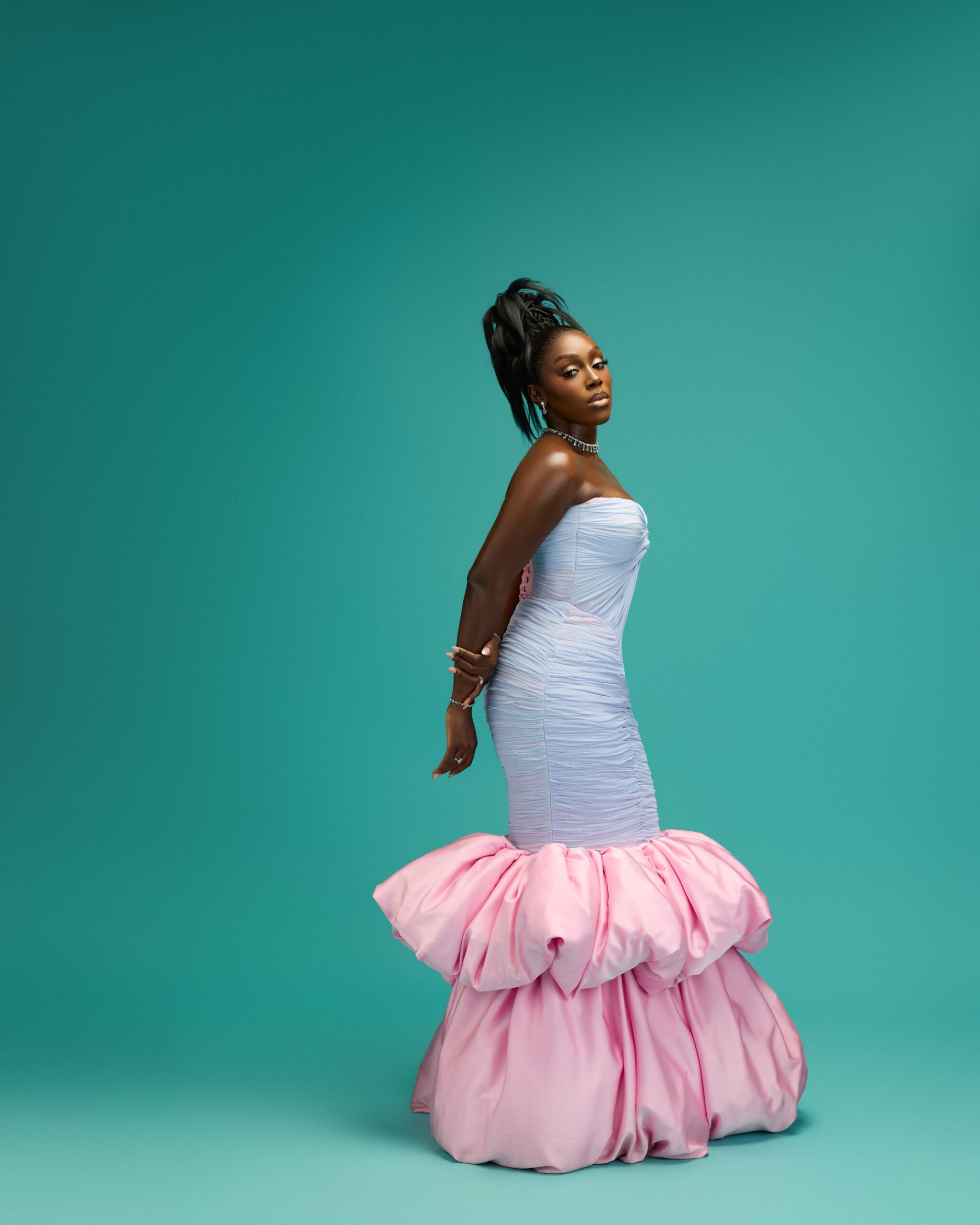 Davita Omoniyi posing in a strapless ice blue ruched gown with a pink bubblegum train against a teal backdrop.