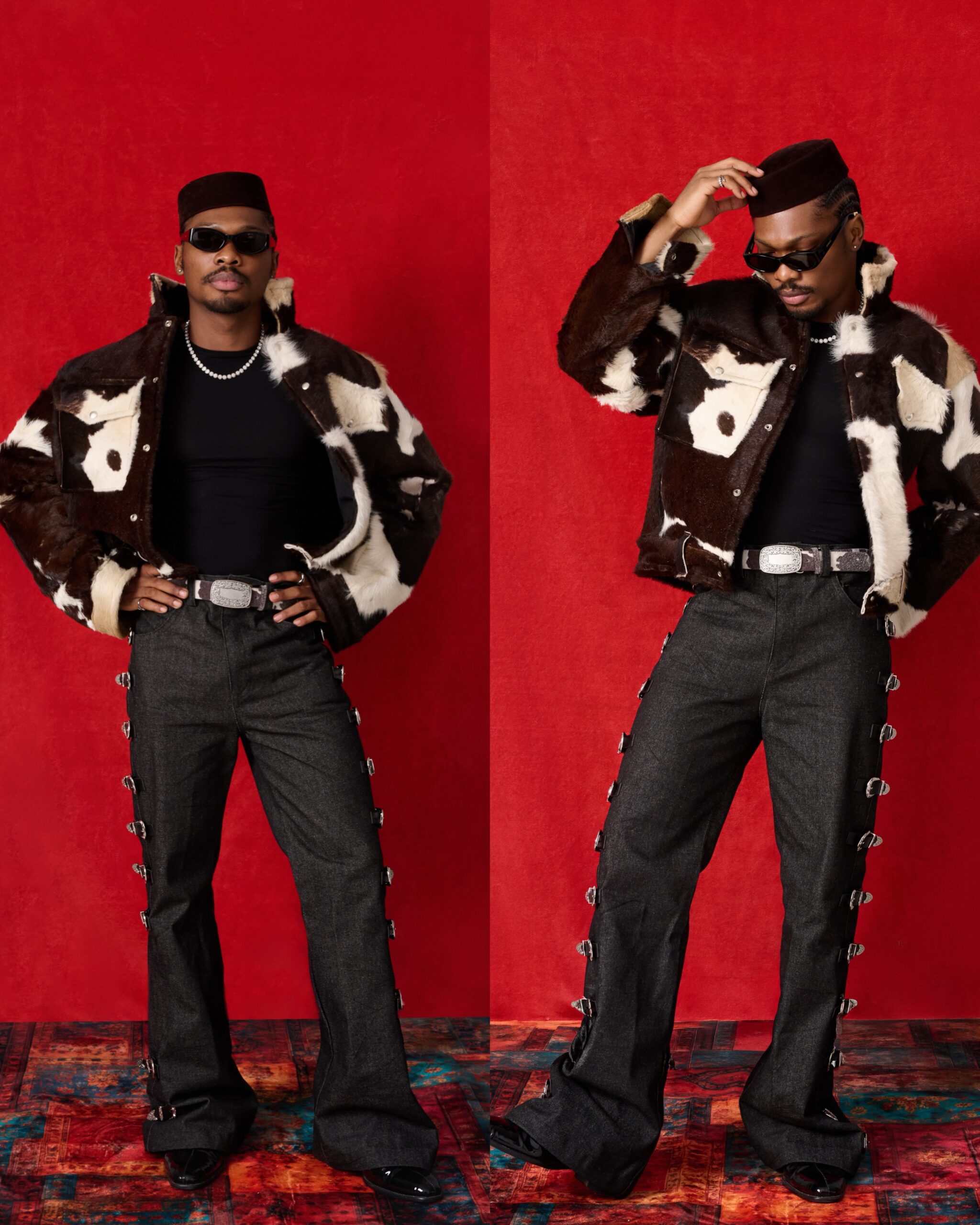 Mike Afolarin wearing a cow-print shearling jacket, black top, dark flare-leg jeans with silver buckles, and a velvet cap.