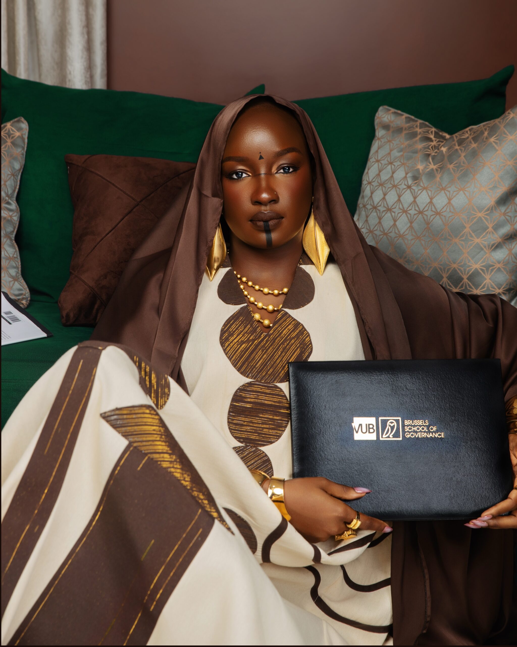 Saskay leaning her chin on her hand over a stack of books wearing gold bangles and a kaftan.