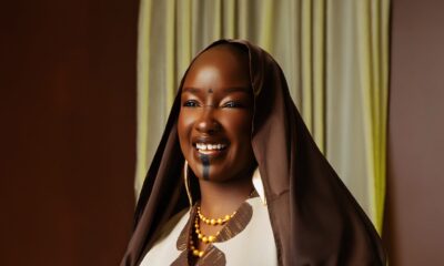 Saskay holding a stack of books wearing the off-white Hertunba Nola Kaftan with brown Aso-Oke appliques and a silk veil.