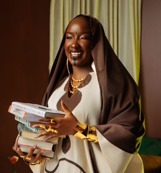 Saskay holding a stack of books wearing the off-white Hertunba Nola Kaftan with brown Aso-Oke appliques and a silk veil.