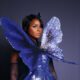 Janelle Monáe wearing a blue sequin gown with oversized butterfly wings across the chest.