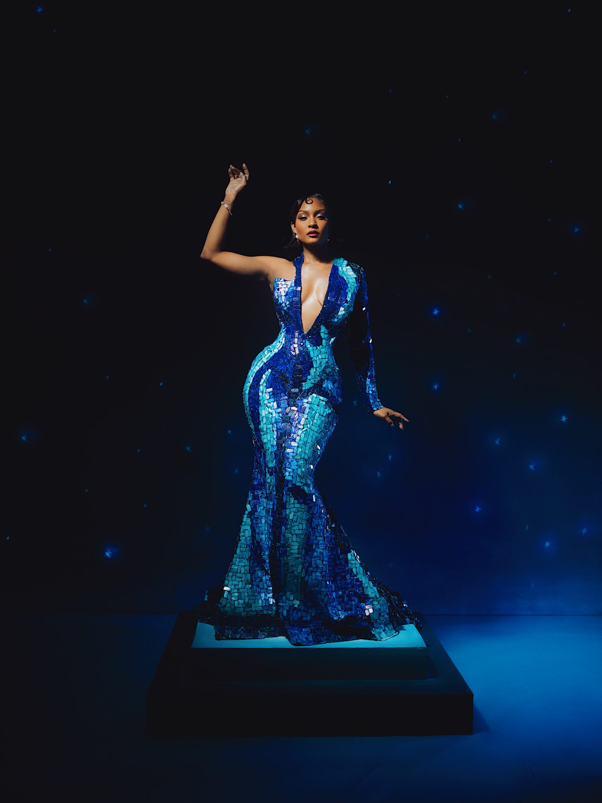 Osas Ighodaro posing on a pedestal in a floor-length mermaid blue mosaic gown by House of Marvee.