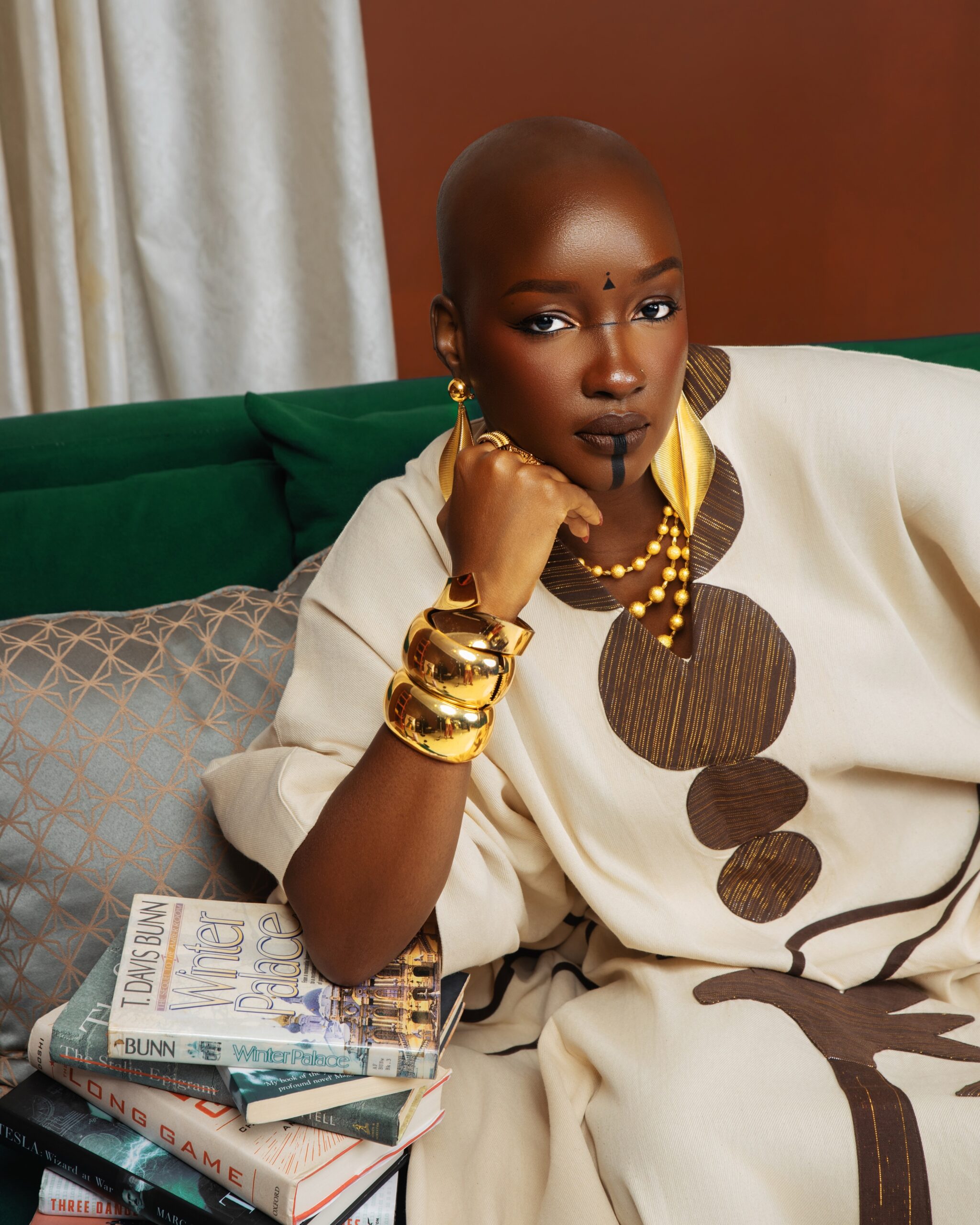 Saskay looking down at her diploma case wearing a chocolate silk veil, gold bangles, and a kaftan.