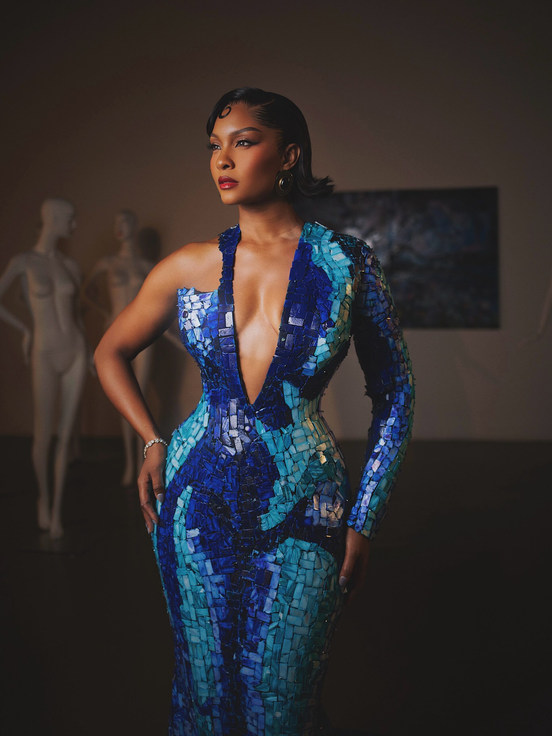 Osas Ighodaro wearing a deep plunge blue mother-of-pearl mosaic gown with one long sleeve.