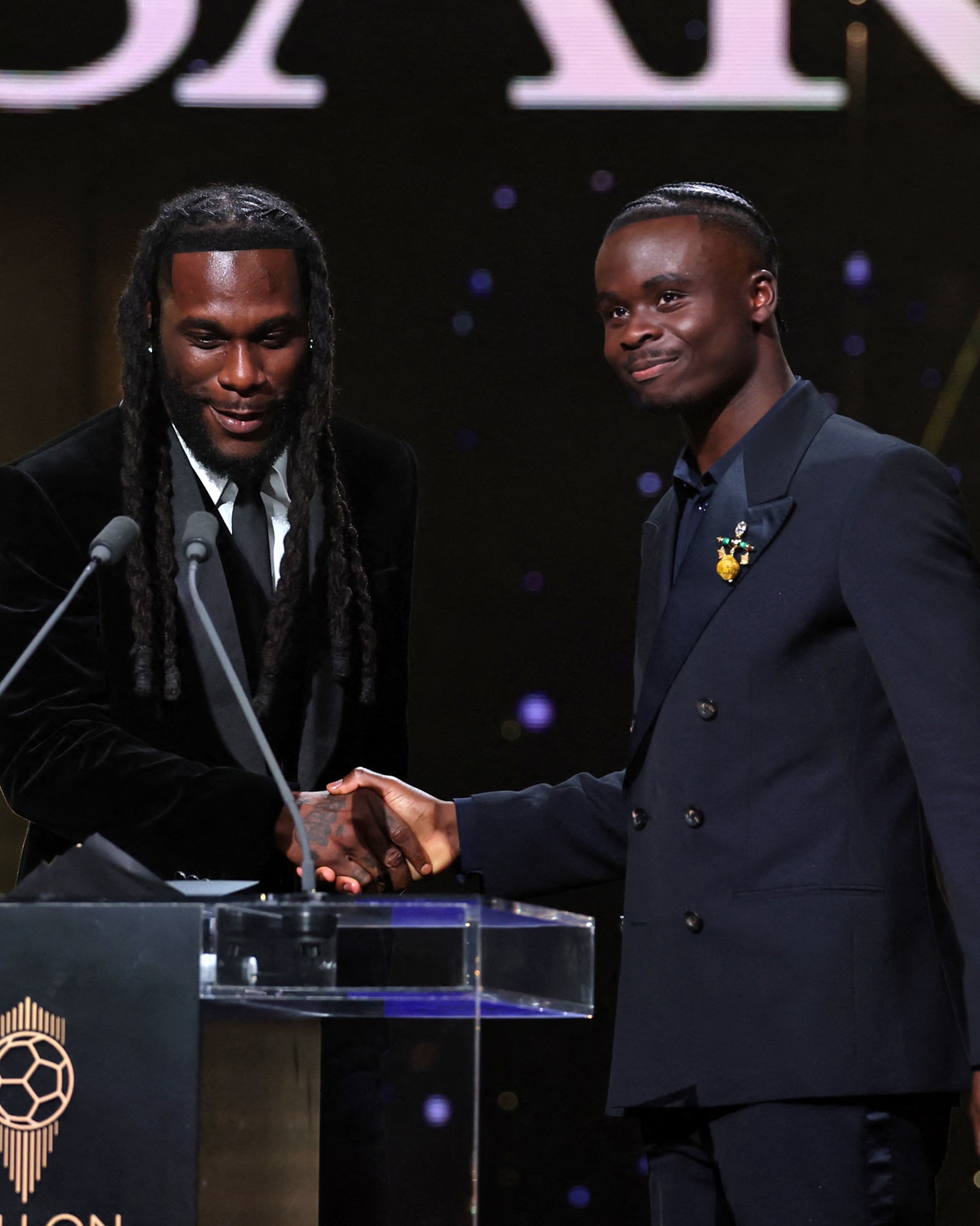 Burna Boy shaking hands with Bukayo Saka at the podium during the 2026 Ballon d’Or ceremony in London.