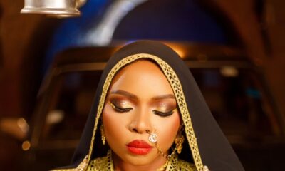 Yemi Alade showing gold hand jewelry, coin necklace, red lipstick, and nose ring chain in the Alhaja video.