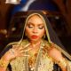 Yemi Alade showing gold hand jewelry, coin necklace, red lipstick, and nose ring chain in the Alhaja video.