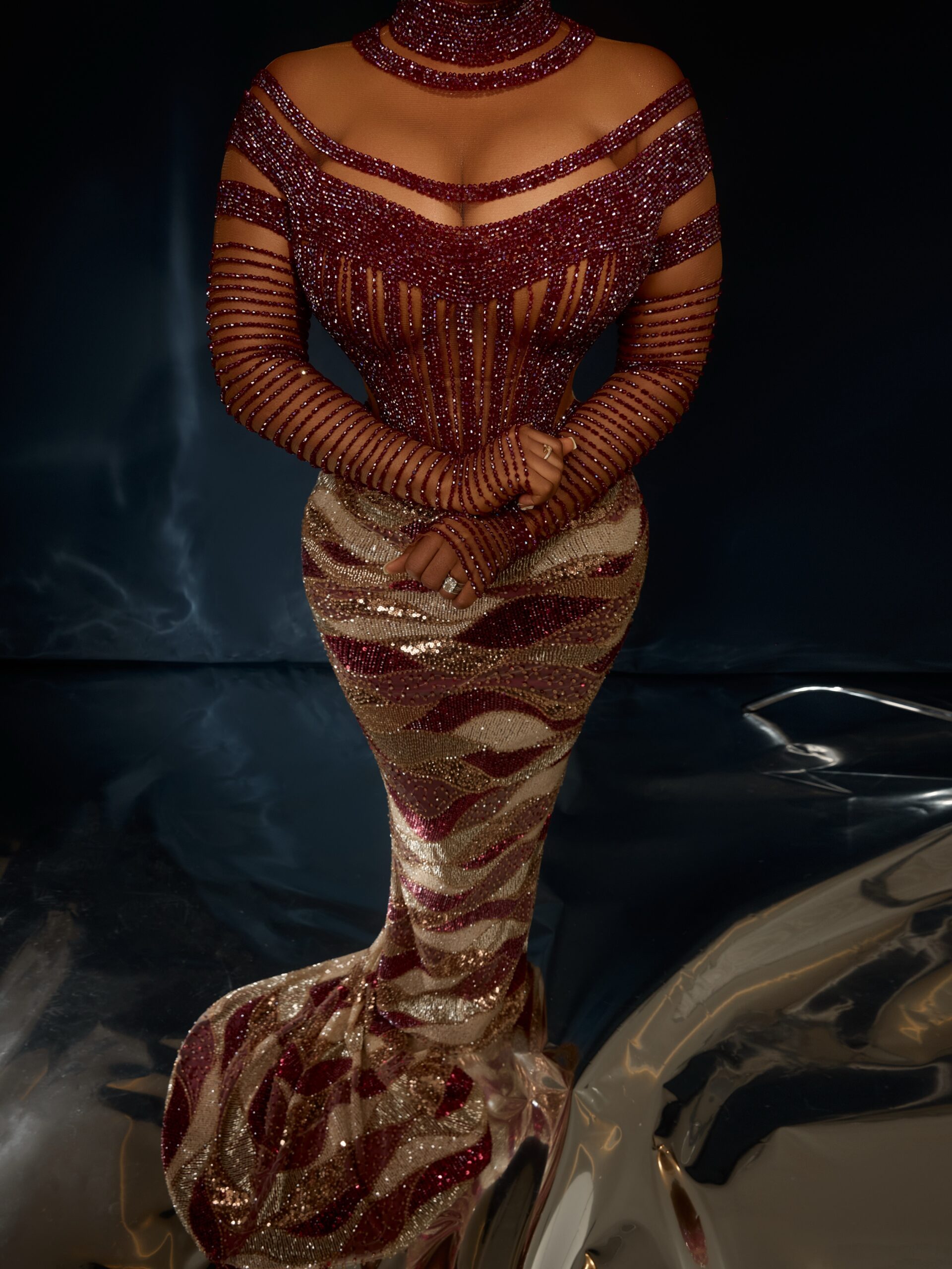 Sheer corset bodice with vertical wine red crystal lines, illusion sweetheart neckline, high neck collar, and a wave-patterned gold sequin skirt.