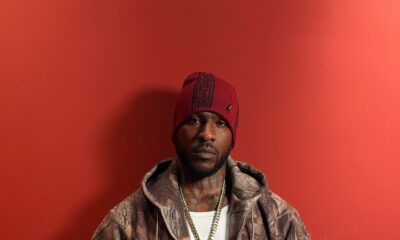 Skepta wearing a camouflage zip-up jacket and Supreme beanie holding a clear vinyl copy of his album The Fork and Knife against a red background.