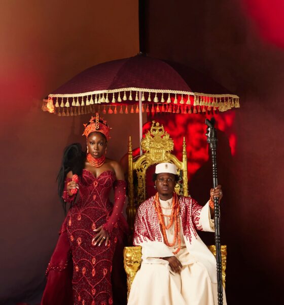 Zlatan Ibile holding a wooden staff seated on a gold throne beneath a tasseled umbrella next to Davita Omoniyi in Edo bridal attire.