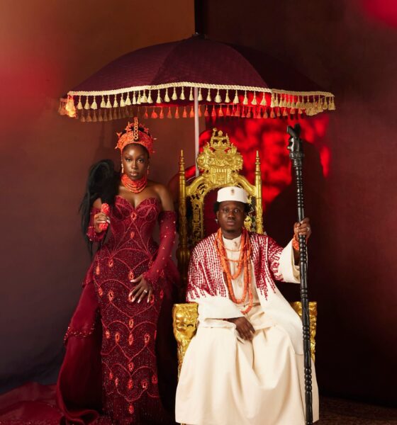 Zlatan Ibile holding a wooden staff seated on a gold throne beneath a tasseled umbrella next to Davita Omoniyi in Edo bridal attire.