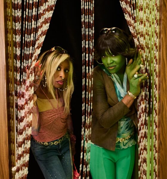 Cynthia Erivo and Ayoade Bamgboye posing behind wooden beaded door curtains for SNL UK Nigerian Wicked sketch.