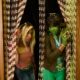 Cynthia Erivo and Ayoade Bamgboye posing behind wooden beaded door curtains for SNL UK Nigerian Wicked sketch.
