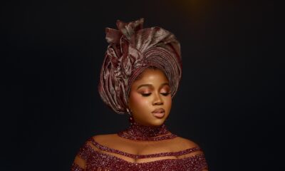 Veekee James wearing a high-neck wine red crystal choker, sheer illusion corset bodice, and pleated metallic dusty rose gele.