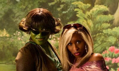 Cynthia Erivo wearing dark-rooted blonde side bangs with Ayoade Bamgboye in sunglasses and green body paint in front of a retro painted backdrop.