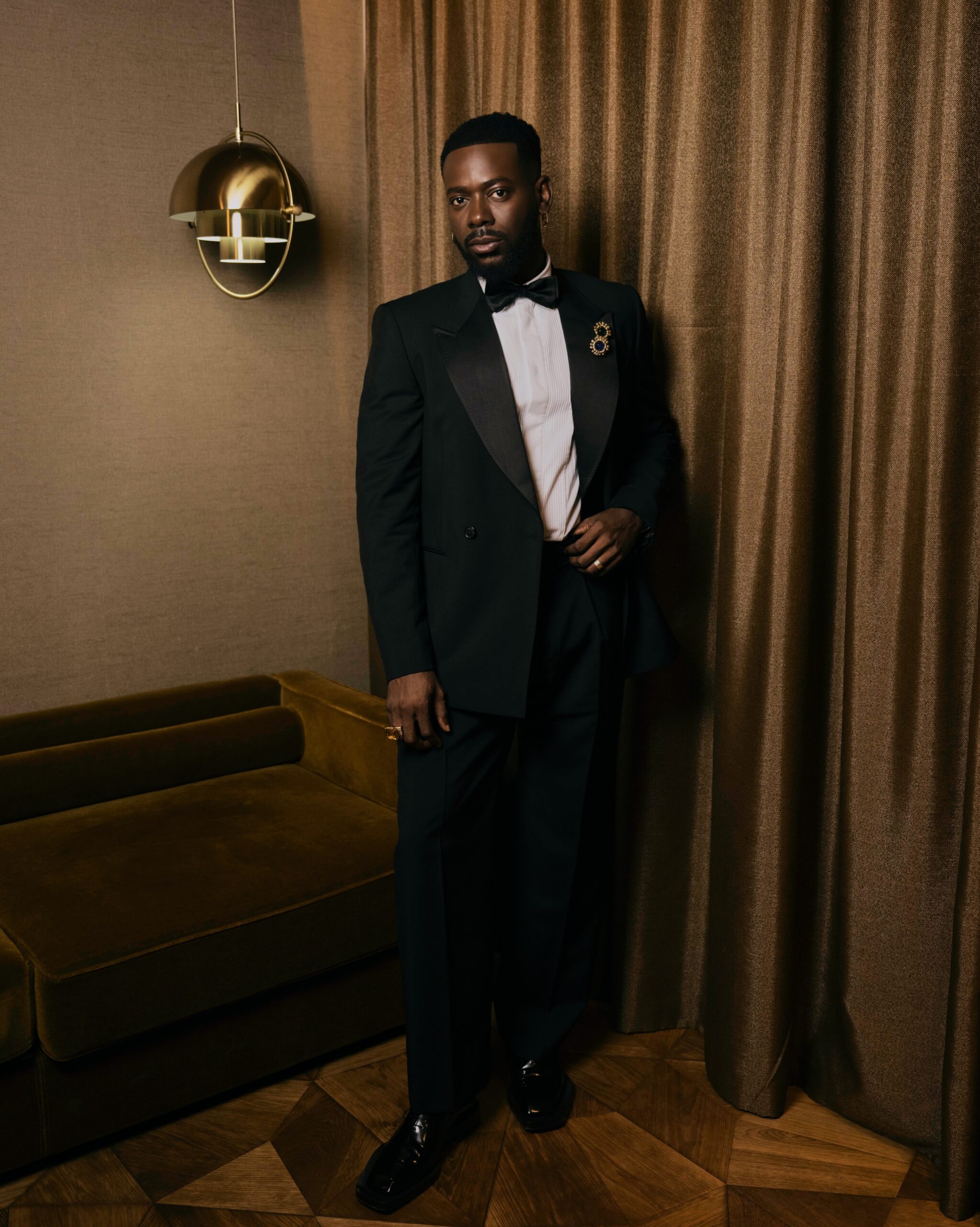 Adekunle Gold wearing a black double-breasted tuxedo, pleated white shirt, black bow tie, and patent shoes.