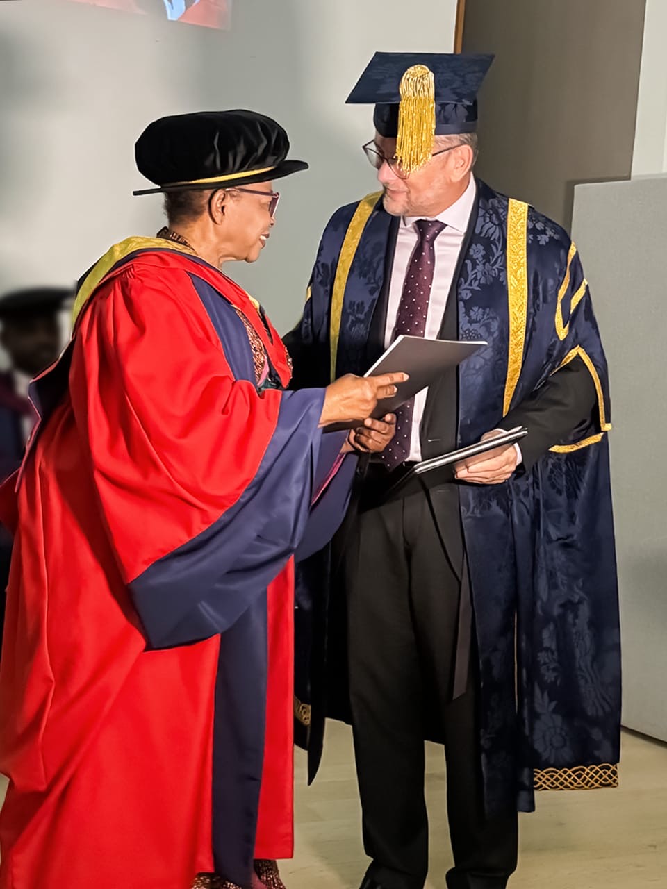 Folorunso Alakija in a red doctoral gown receiving her honorary degree certificate from Vice-Chancellor Professor David Cole.