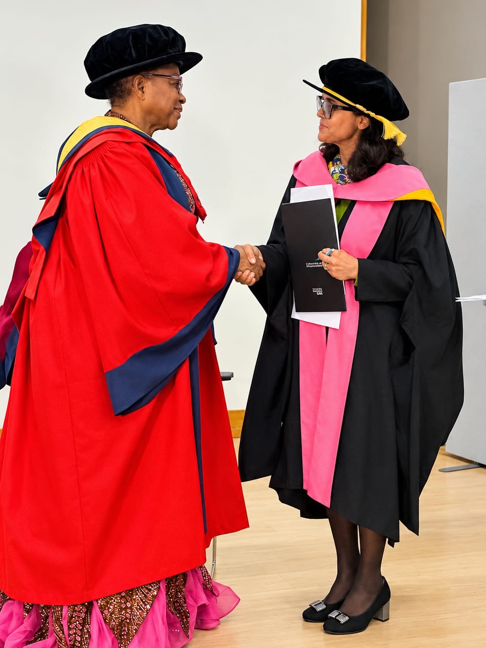 Folorunso Alakija shaking hands with Dean of Faculty Professor Debarpita Bardhan-Correia in academic attire.