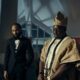 Phyno in a black suit beside Wande Coal in traditional Yoruba Agbada and Fila cap in the Ndewo music video directed by TG Omori.