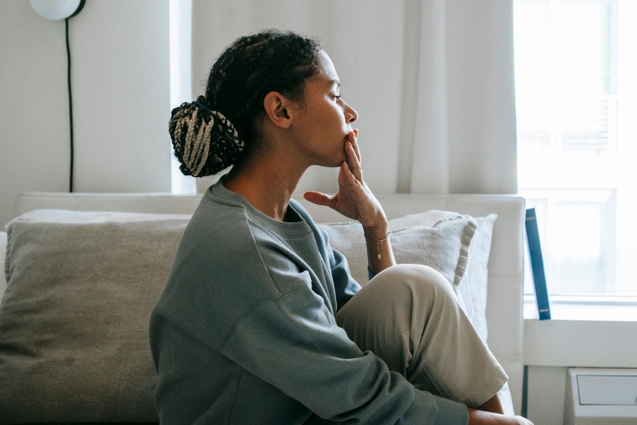 A thoughtful young woman sits in a relaxed pose in a serene bedroom, reflecting peacefully. Photo credit: Alex Green/Pexels.