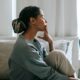 A thoughtful young woman sits in a relaxed pose in a serene bedroom, reflecting peacefully. Photo credit: Alex Green/Pexels.