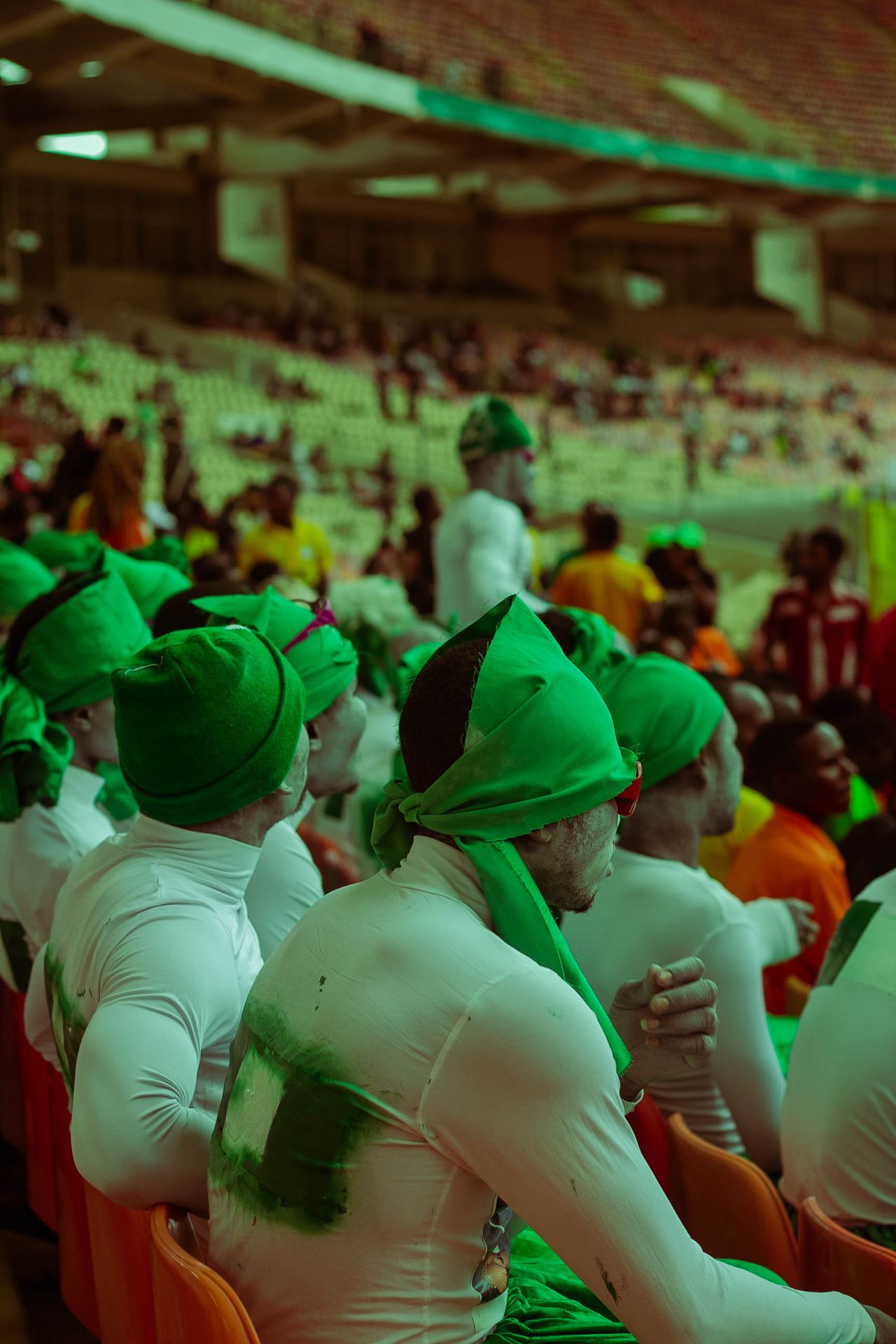 A lively festival crowd in green costumes, sitting in grandstands enjoying a performance.